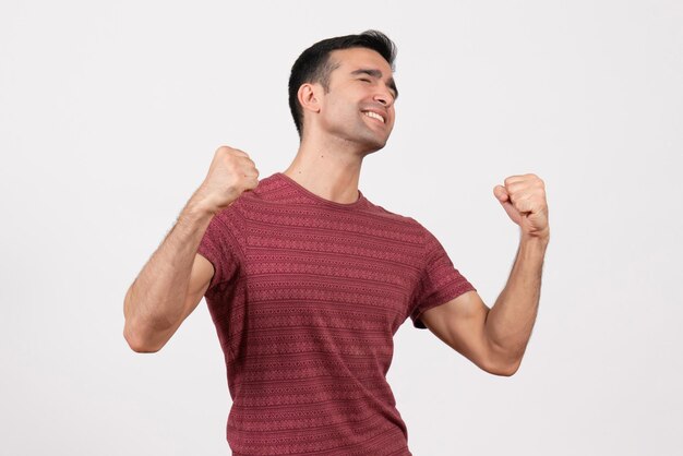 Vooraanzicht jonge man in donkerrood t-shirt staan en verheugen zich op witte achtergrond