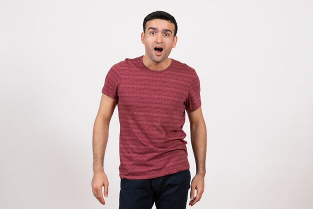 Vooraanzicht jonge man in donkerrood t-shirt staande met verbaasde uitdrukking op witte achtergrond