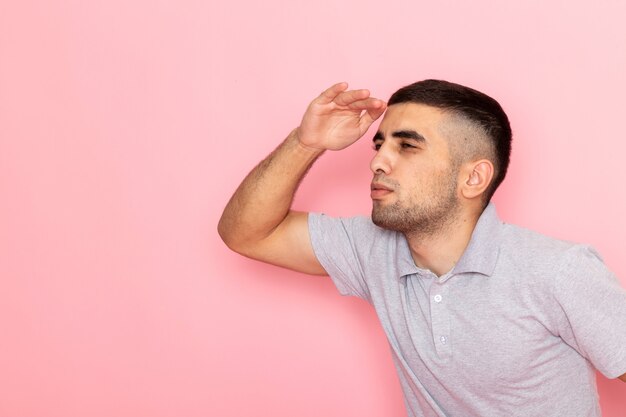 Vooraanzicht jonge man in grijs shirt op zoek in de verte op roze