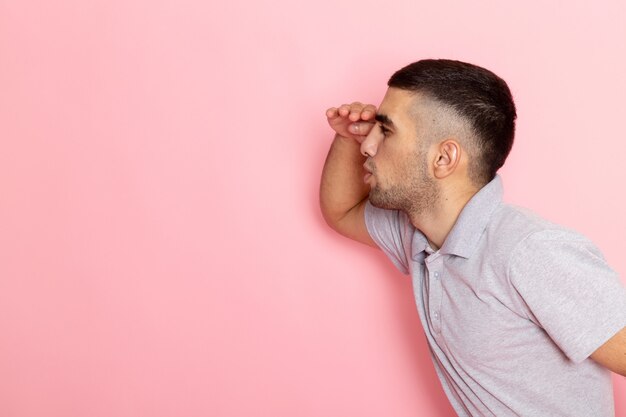 Vooraanzicht jonge man in grijs shirt op zoek in de verte op roze