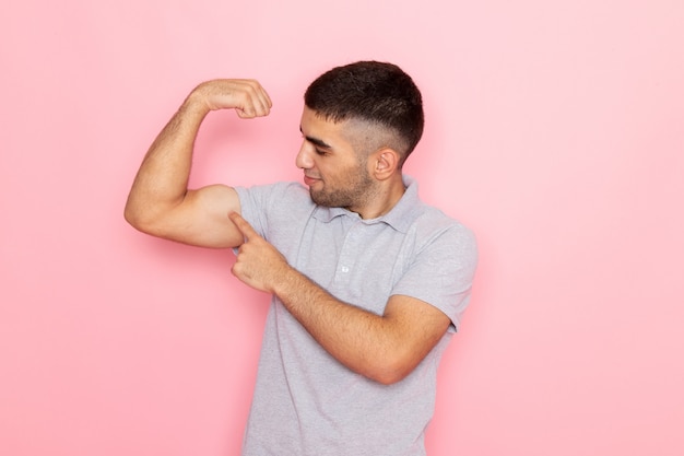 Gratis foto vooraanzicht jonge man in grijs shirt poseren buigen lachend op roze