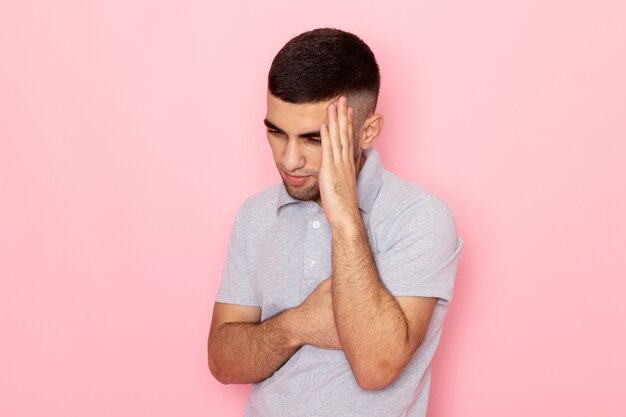 Vooraanzicht jonge man in grijs shirt poseren met denken expressie op roze