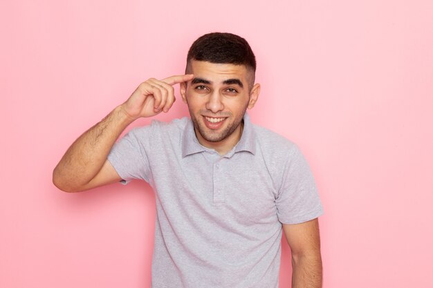 Vooraanzicht jonge man in grijs shirt poseren met een glimlach op roze