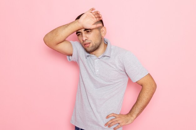 Vooraanzicht jonge man in grijs shirt poseren met vermoeide uitdrukking op roze