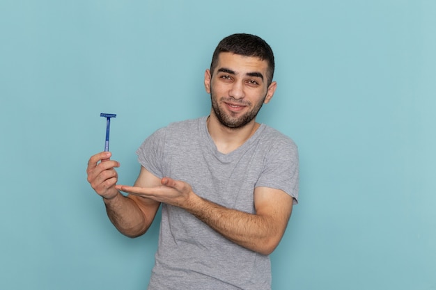 Vooraanzicht jonge man in grijs t-shirt met scheermes met lichte glimlach op blauw scheren baard mannelijk haar schuim kleur