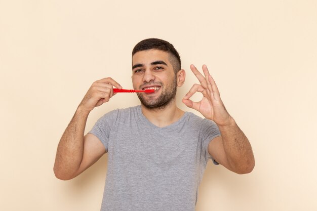 Vooraanzicht jonge man in grijs t-shirt zijn tanden schoonmaken en glimlachen op beige