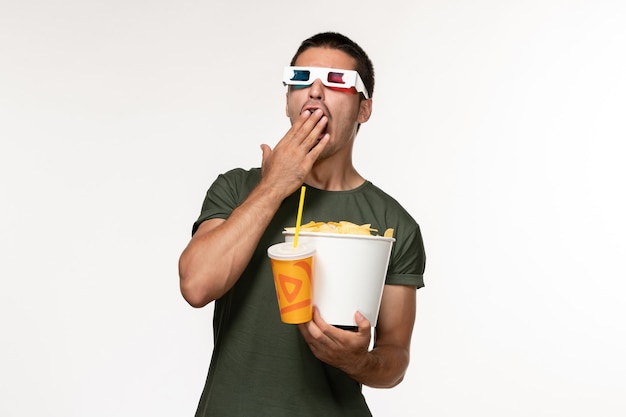 Vooraanzicht jonge man in groen t-shirt met aardappel cips en frisdrank in d zonnebril geeuwen op witte muur film mannelijke eenzame film