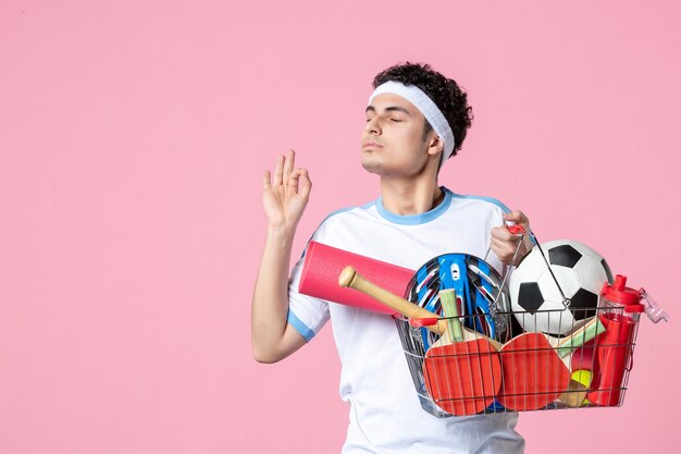 Vooraanzicht jonge man in sportkleding met mand vol met sport dingen roze muur