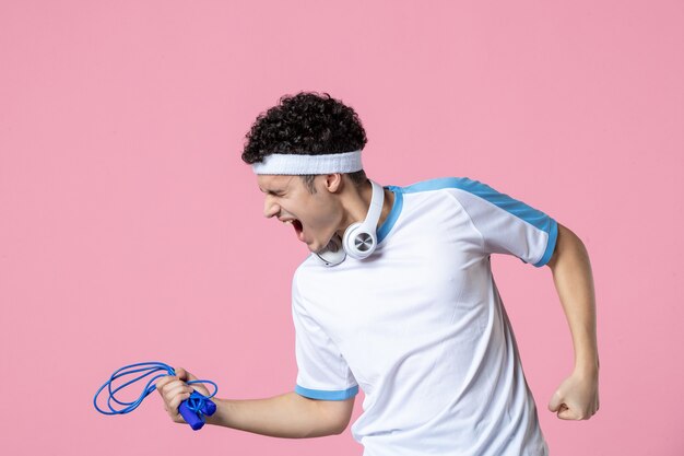 Vooraanzicht jonge man in sportkleding met springtouw op de roze muur