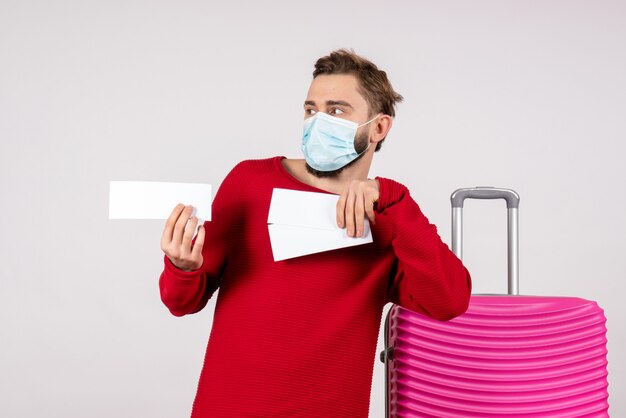 Vooraanzicht jonge man in steriel masker met kaartjes op witte muur reis covid-vlucht reis kleur emotie virus