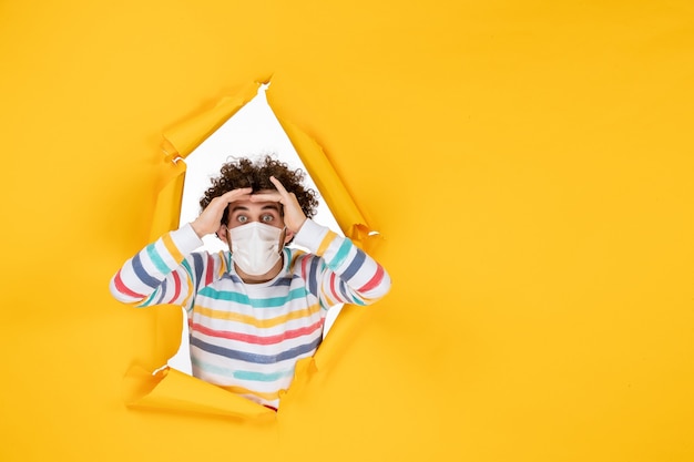 Gratis foto vooraanzicht jonge man in steriel masker op gele covid-gezondheid menselijke pandemische virusfoto