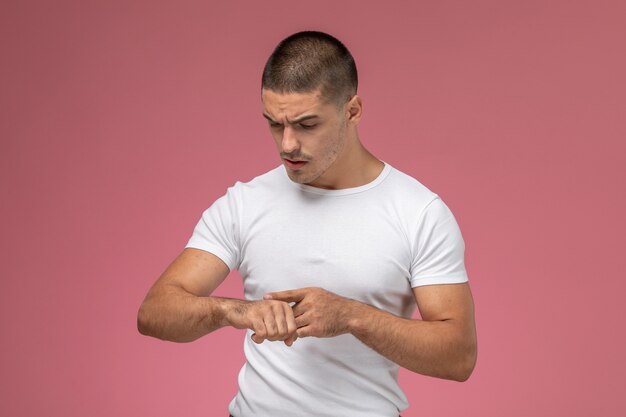 Vooraanzicht jonge man in wit overhemd kijken naar zijn pols op de roze achtergrond