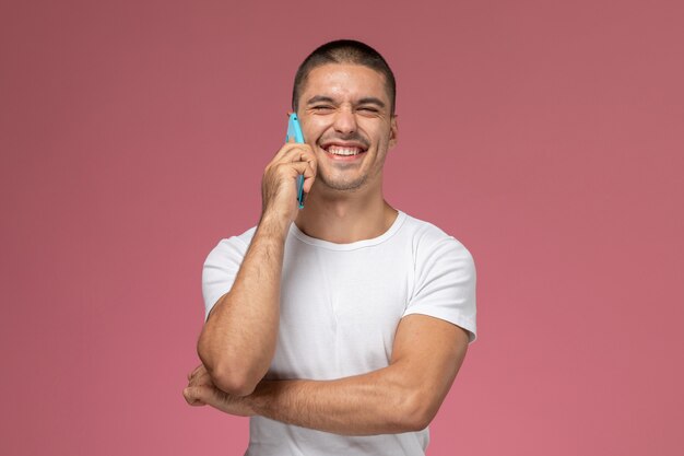 Vooraanzicht jonge man in wit overhemd praten aan de telefoon en lachen op roze achtergrond