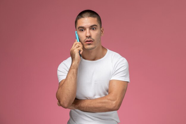 Vooraanzicht jonge man in wit overhemd praten aan de telefoon met gestoorde uitdrukking op roze achtergrond