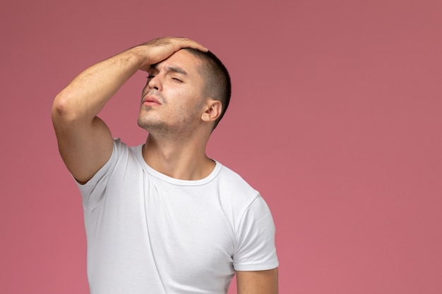 Vooraanzicht jonge man in wit t-shirt benadrukt en houdt zijn hoofd op roze achtergrond