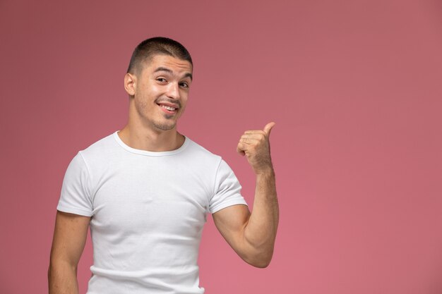 Vooraanzicht jonge man in wit t-shirt glimlachend en wijzen op roze bureau