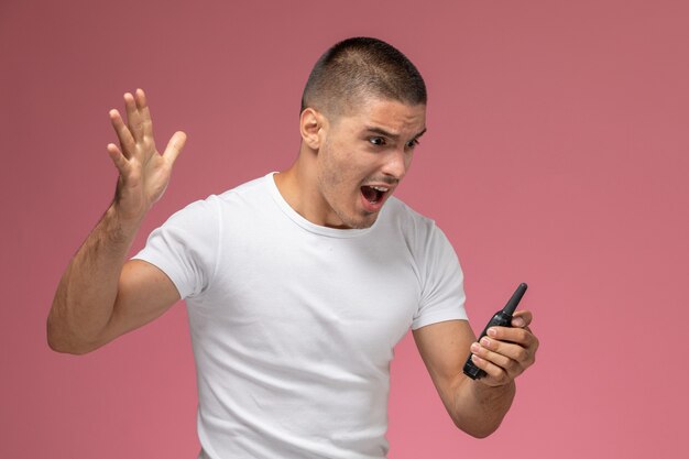 Vooraanzicht jonge man in wit t-shirt met walkie-talkie en schreeuwen op roze achtergrond