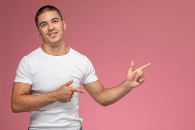 Vooraanzicht jonge man in wit t-shirt poseren met glimlach wijzen op roze achtergrond
