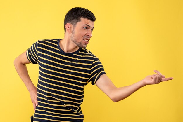 Vooraanzicht jonge man in zwart-wit gestreept t-shirt hand op een taille zetten gele geïsoleerde achtergrond