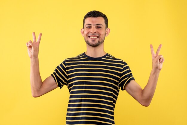 Vooraanzicht jonge man in zwart-wit gestreept t-shirt overwinning zingen op gele geïsoleerde achtergrond