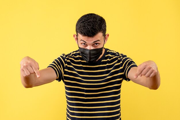 Vooraanzicht jonge man in zwart-wit gestreepte t-shirt wijzend op de vloer op gele geïsoleerde achtergrond