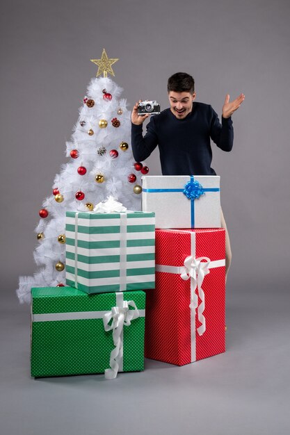 Vooraanzicht jonge man met cadeautjes en camera op het grijs