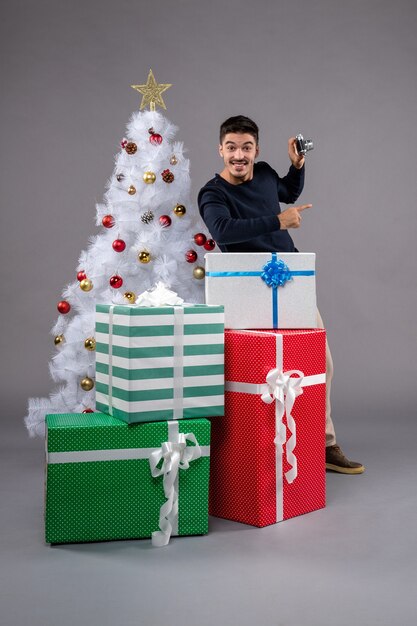 Vooraanzicht jonge man met camera en cadeautjes op het grijs