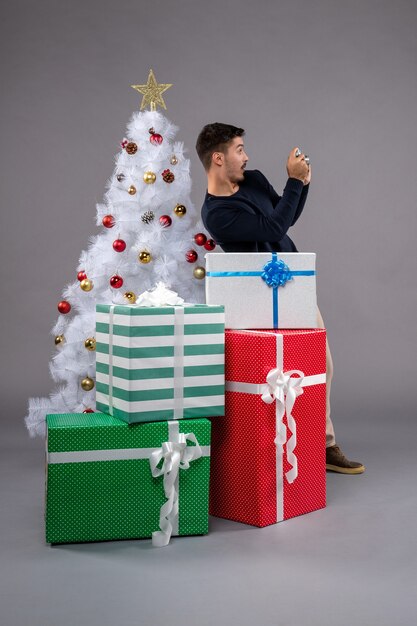 Vooraanzicht jonge man met camera en cadeautjes op het grijs