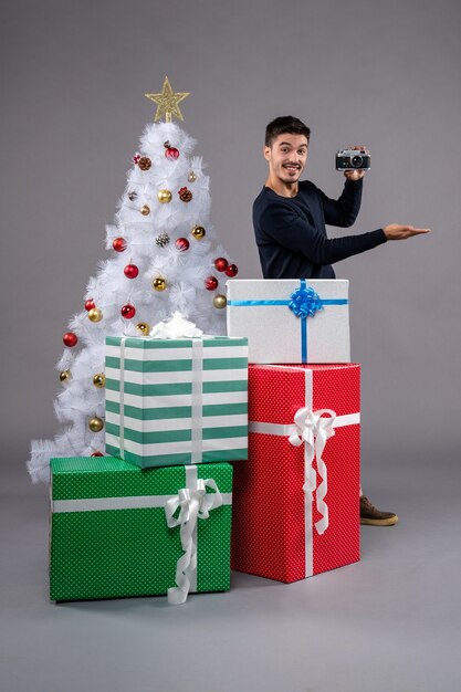 Vooraanzicht jonge man met camera en cadeautjes op het grijs