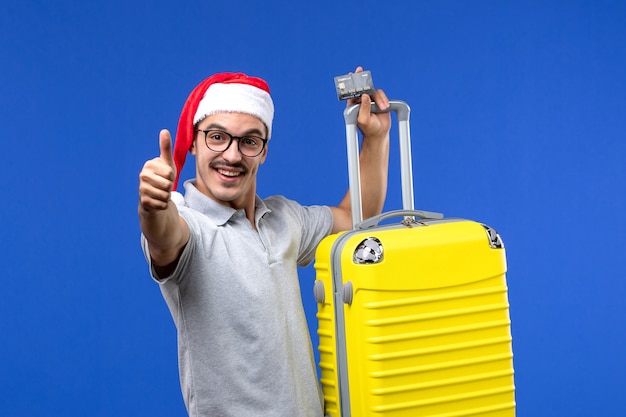 Gratis foto vooraanzicht jonge man met gele zak bankkaart op blauwe muur reis vakantie emoties