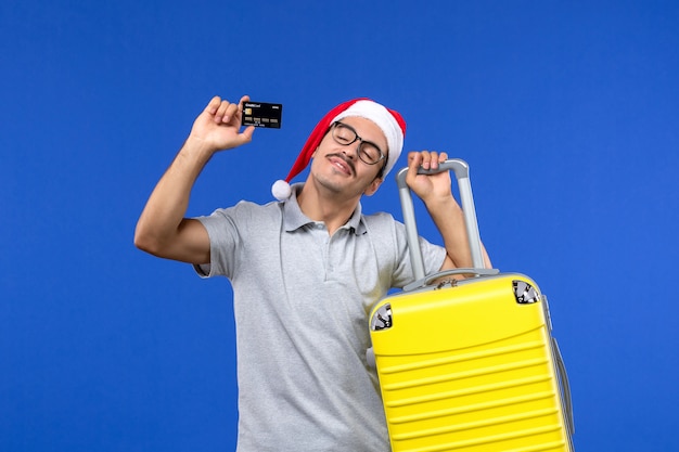 Vooraanzicht jonge man met gele zak bankkaart op blauwe muur vakantie vliegtuig vlucht