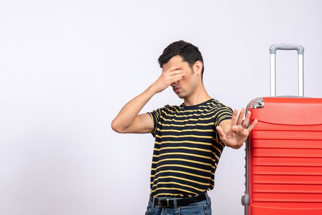 Vooraanzicht jonge man met gestreept t-shirt en koffer die betrekking hebben op oog met hand stopbord maken