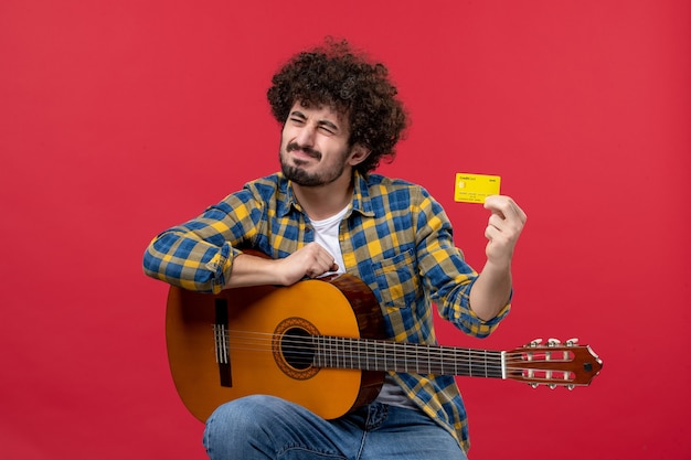 Vooraanzicht jonge man met gitaar met gele bankkaart op rode muur kleur prestatie applaus live concert