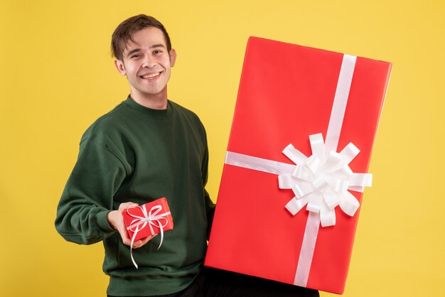 Vooraanzicht jonge man met groene trui met grote en kleine geschenken staande op geel