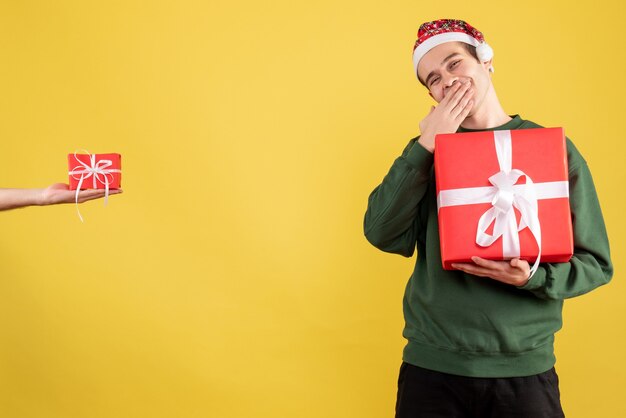 Vooraanzicht jonge man met grote gift menselijke hand met cadeau staande op geel