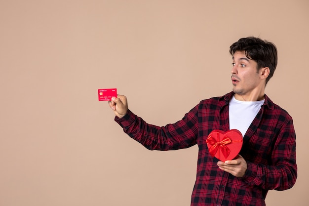 Vooraanzicht jonge man met hartvormig cadeau en bankkaart op bruine muur