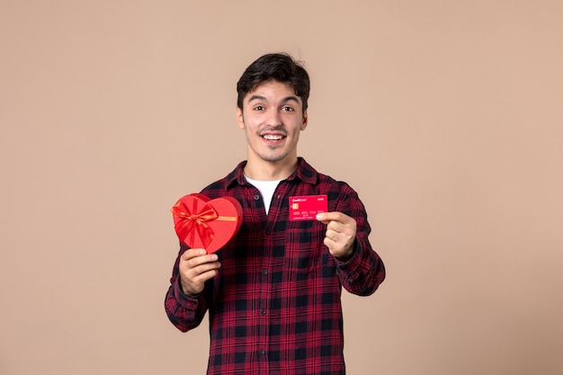Vooraanzicht jonge man met hartvormig cadeau en bankkaart op bruine muur
