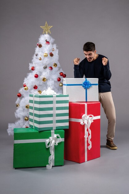 Vooraanzicht jonge man met kerstcadeautjes op het grijs