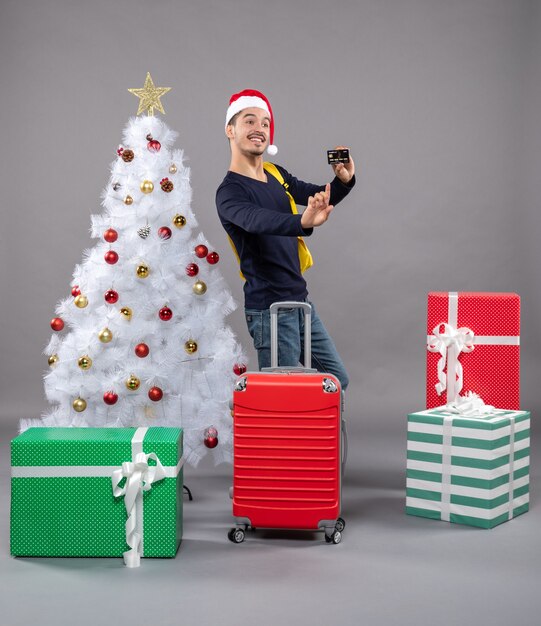 Vooraanzicht jonge man met kerstmuts en koffer met een kaart op grijs geïsoleerd
