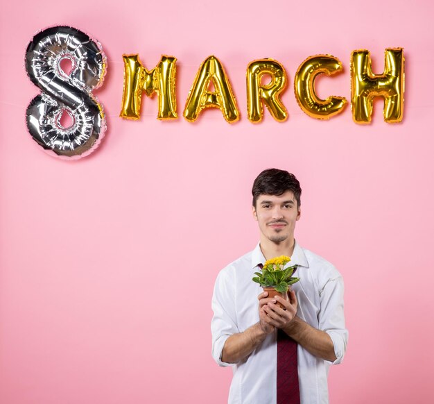 Vooraanzicht jonge man met kleine bloem in pot met maart decoratie op roze achtergrond huwelijksfeest gelijkheid vrouwelijke vrouwen dag aanwezig kleur man