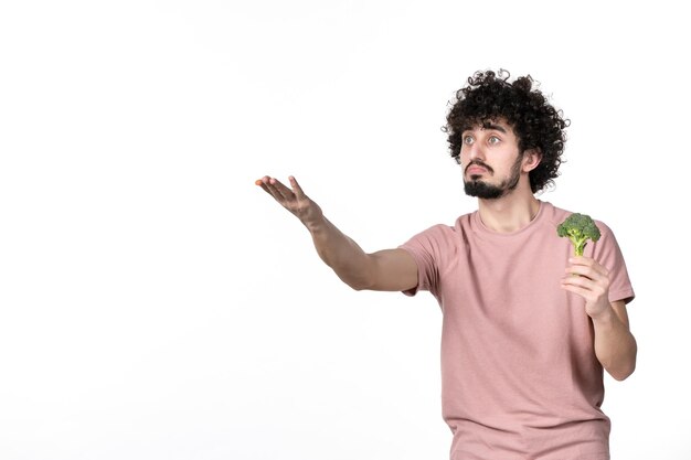 Vooraanzicht jonge man met kleine groene broccoli en wijzend op wit