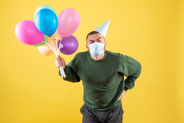 Vooraanzicht jonge man met kleurrijke ballonnen op een gele achtergrond