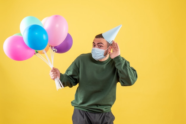 Vooraanzicht jonge man met kleurrijke ballonnen op een gele achtergrond