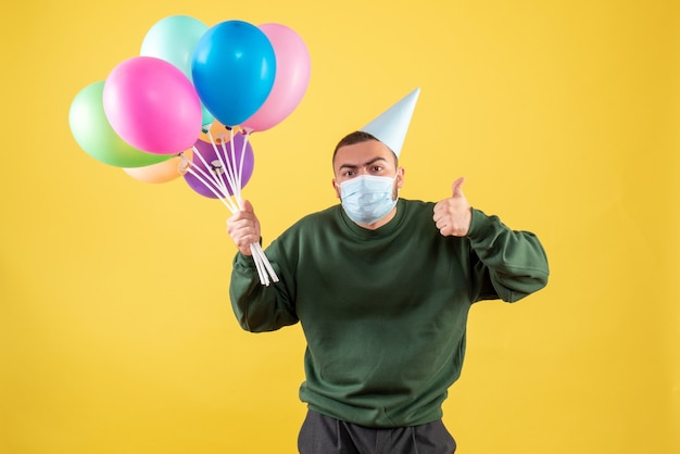 Vooraanzicht jonge man met kleurrijke ballonnen op een gele achtergrond