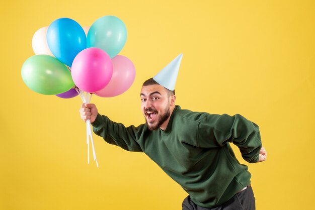 Vooraanzicht jonge man met kleurrijke ballonnen op een gele achtergrond