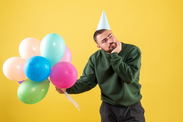 Vooraanzicht jonge man met kleurrijke ballonnen op geel