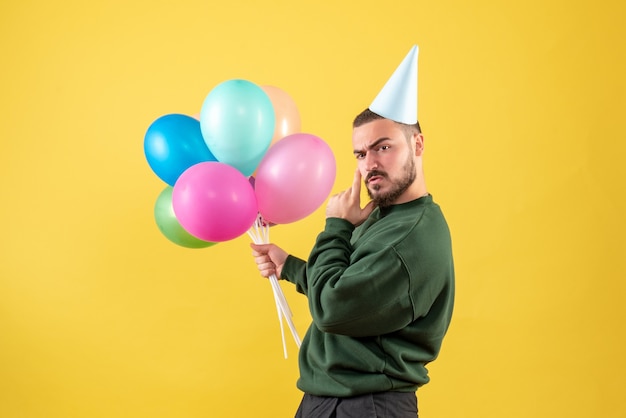 Vooraanzicht jonge man met kleurrijke ballonnen op gele achtergrond