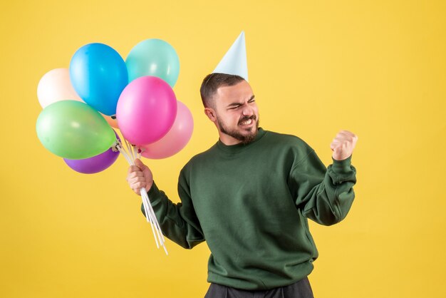 Vooraanzicht jonge man met kleurrijke ballonnen op gele achtergrond