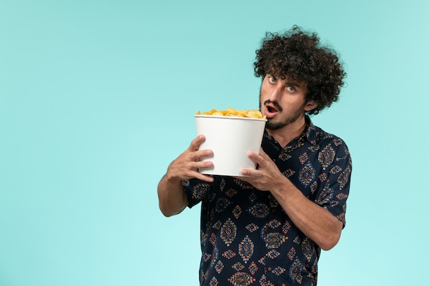 Vooraanzicht jonge man met mand met aardappel cips op de blauwe muur mannelijke film bioscoop film afstandsbediening