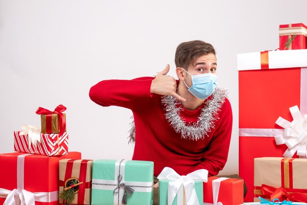 Vooraanzicht jonge man met masker bellen me telefoon teken zitten rond xmas geschenken